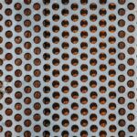 High angle view of a perforated metal sheet against a wooden surface, showcasing a unique pattern.